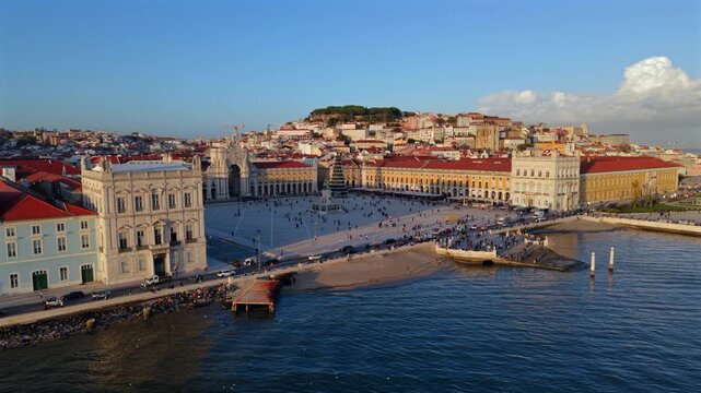 Wide aerial view of Praca do Comercio in Lisbon with yellow facades, open square and calm Tagus River, showing classic Portuguese architecture, city life and coastal atmosphere