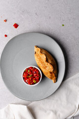 Overhead view of baked empanadas with pico de gallo on a grey plate, top view of empanadas and salsa, bolivian salte&ntilde;a with chopped tomato sauce