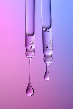 Two Clear glass pipettes with drops of cosmetic product falling down. 
