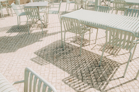 Empty terrace chairs casting striped shadows on pavement
