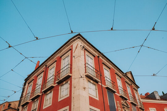 Red building corner under blue sky framed by electric cables