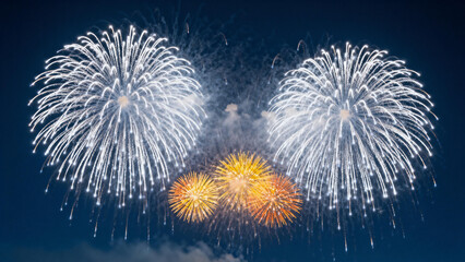 Vibrant fireworks explode in the night sky, featuring large white bursts and smaller golden bursts against a dark blue background.