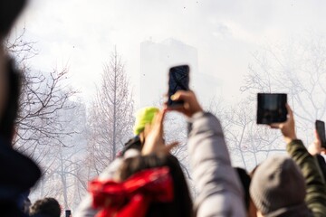 People Taking Photos at Outdoor Event with Smoke and Phones Raised  
