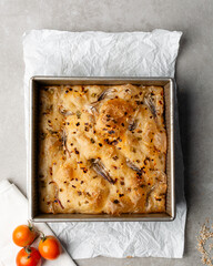 overhead view of onion and scallion focaccia in a baking tin, top view of airy bubbly onion focaccia on a cement countertop	