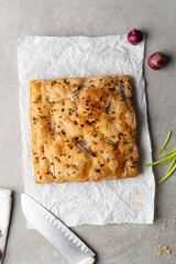 overhead view of onion and scallion focaccia on parchment paper, top view of airy bubbly onion focaccia on a cement countertop