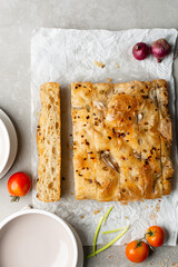 overhead view of slices of onion and scallion focaccia on parchment paper, top view of airy bubbly onion focaccia on a cement countertop