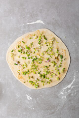 Overhead view of scallions on chinese pancake dough on grey countertop, process of making homemade scallion pancakes or cong you bing