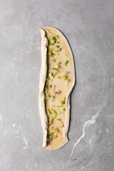 Overhead view of raw chinese scallion pancakes being rolled on grey countertop, top view of homemade scallion pancakes being shaped on countertop, process of making cong you bing