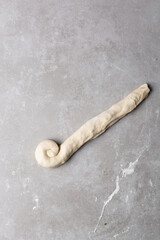 Overhead view of raw chinese scallion pancakes being rolled on grey countertop, top view of homemade scallion pancakes being shaped on countertop, process of making cong you bing