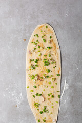 Overhead view of scallions on chinese pancake dough on grey countertop, process of making homemade scallion pancakes or cong you bing