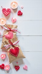 Decorative gift bags with heart ornaments and burning candles on a rustic white wood surface. Valentine's Day celebration.