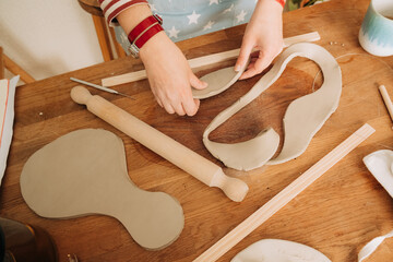 Arranging and shaping clay pieces on craft table with pottery to
