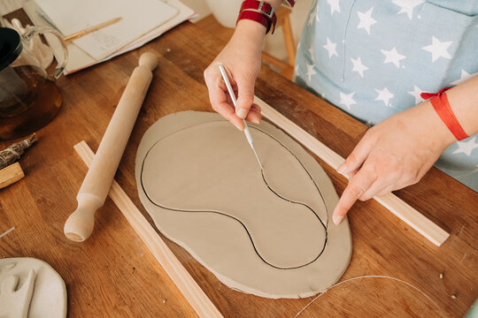 Detail of hands cutting organic shape in clay with precision pot