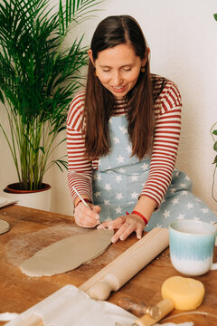 Female artisan carving details into flat clay slab on wooden tab