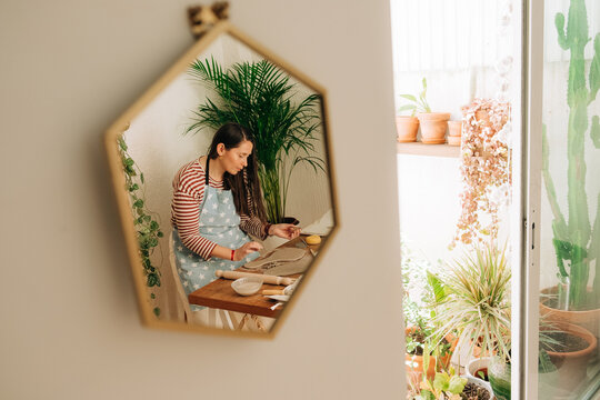 Reflection of woman shaping clay in cozy home pottery studio wit