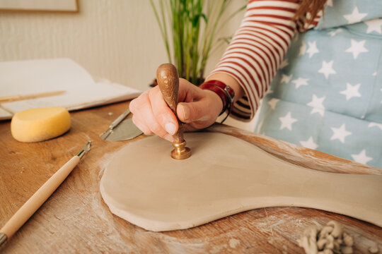 Close-up of stamping design into soft clay on wooden workbench