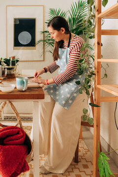 Creative woman shaping clay at home ceramic studio with cozy dec