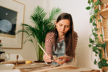 Focused woman carving clay with modeling tool in home pottery st