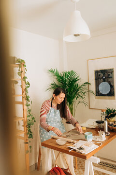 Woman shaping clay on table in warm home pottery studio with pla