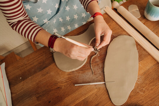 Carving excess clay from slab with sculpting tool in home studio