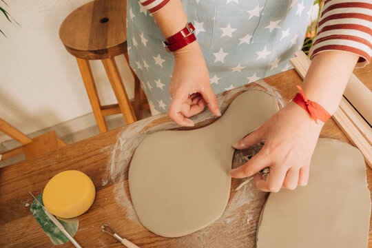 Hands shaping organic clay slab on wooden table in pottery studi