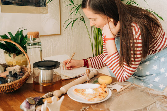 Woman writing in notebook while working on clay craft project