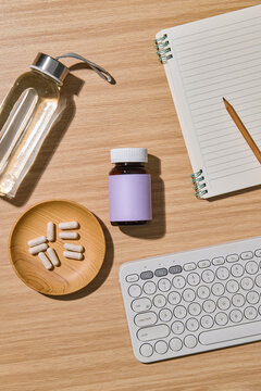 Vitamins and supplements on a wooden desk with a keyboard and notebook