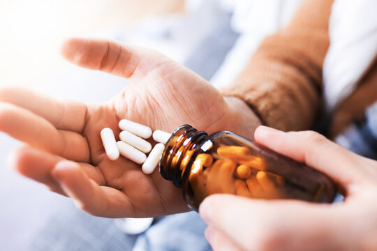 Close up of man hands pouring white capsules from glass bottle into palm. Person taking medicine or supplements.