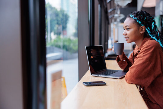 Woman with laptop and coffee looks out window.
