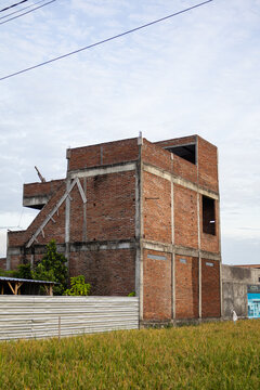 Unfinished brick building under construction with natural light, surrounded by green field and clear sky, providing copy space for real estate development projects