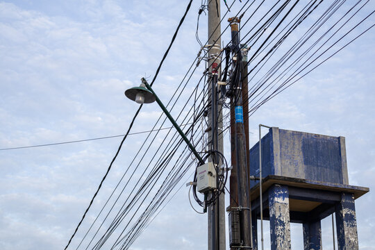 Utility pole laden with tangled electrical wires and a street lamp against a cloudy sky, providing essential infrastructure with copy space