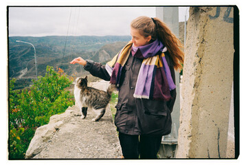 Woman interacts with a cat on a scenic hillside
