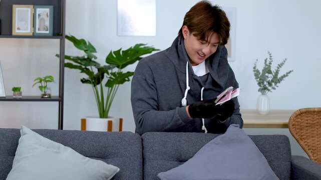 Criminal in Hoodie and Gloves Counting Stolen Cash Behind Sofa