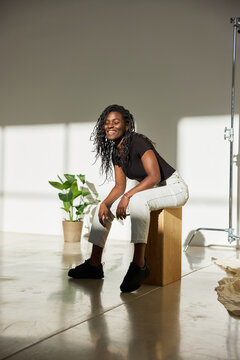 Smiling woman sitting on a wooden block in a bright studio