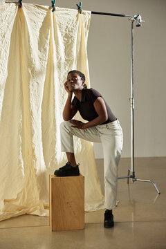 Model poses thoughtfully on a wooden box during studio shoot