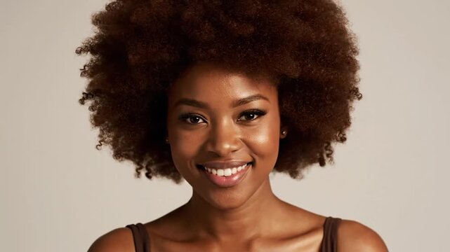 A woman with a large afro smiles warmly, her skin glowing under studio lights