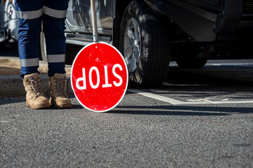A traffic control person with a stop sign, with safety boots and work trousers 
