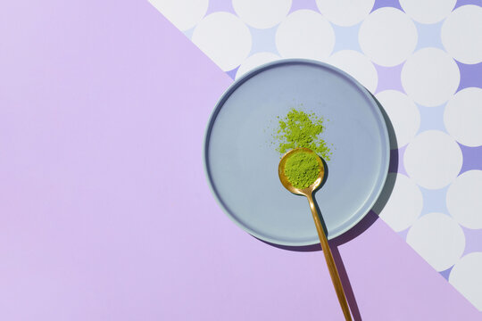 A golden spoon with matcha powder rests on a blue plate