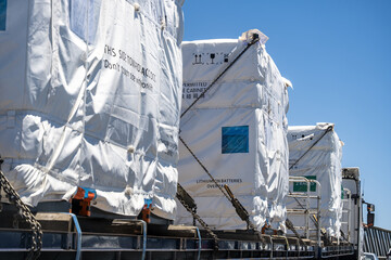 Large industrial cargo units containing lithium battery systems secured on a flatbed truck for transportation. Logistics and freight operation, energy infrastructure supply chains in Australia © Doublelee