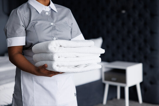 Partial view of maid holding stack of towels in blurred hotel room