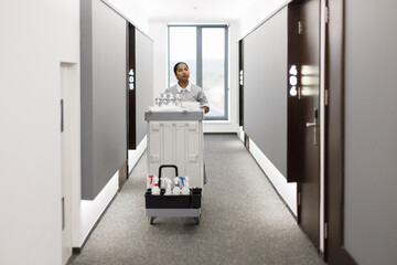Latin maid going with cart and looking at room in hotel hall