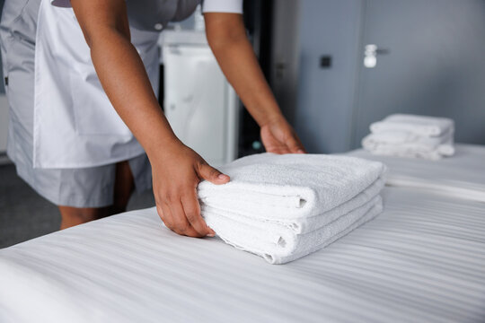 Cropped view of maid putting towels on bed in comfortable hotel room