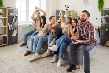 Friends watching football match on TV, celebrating. Fans at home on a sofa clap and laugh, reacting...