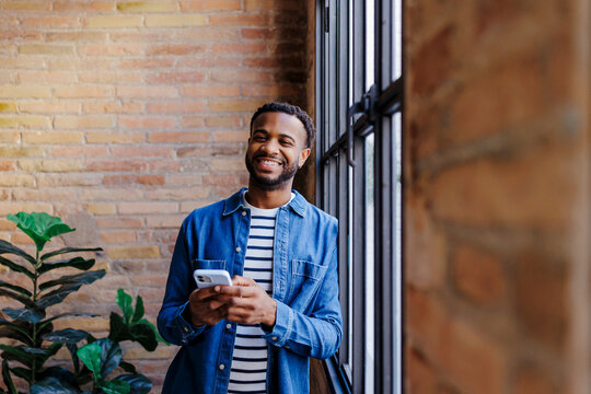 Smiling man holding smartphone while standing near a window at office