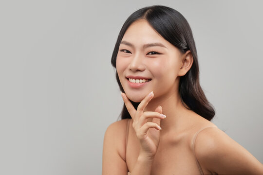 Beautiful Asian woman smiles while touching her chin, studio portrait