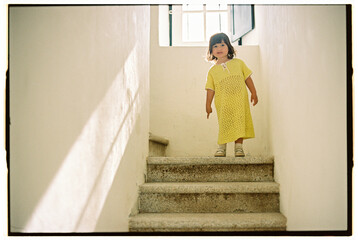 Girl in yellow on sunlit staircase under window light