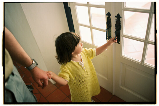 Girl reaching door handle while holding adult's hand