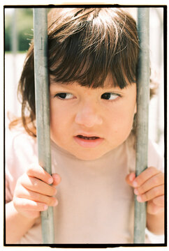 Close-up of child peeking between metal bars in sunlight