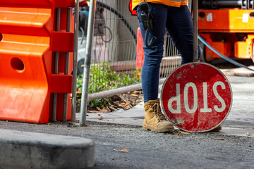 A traffic control person, in a saftey vest, with a stop sign, with safety boots and work trousers 