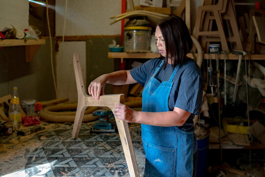 Woman in blue apron sanding or shaping wood in a workshop